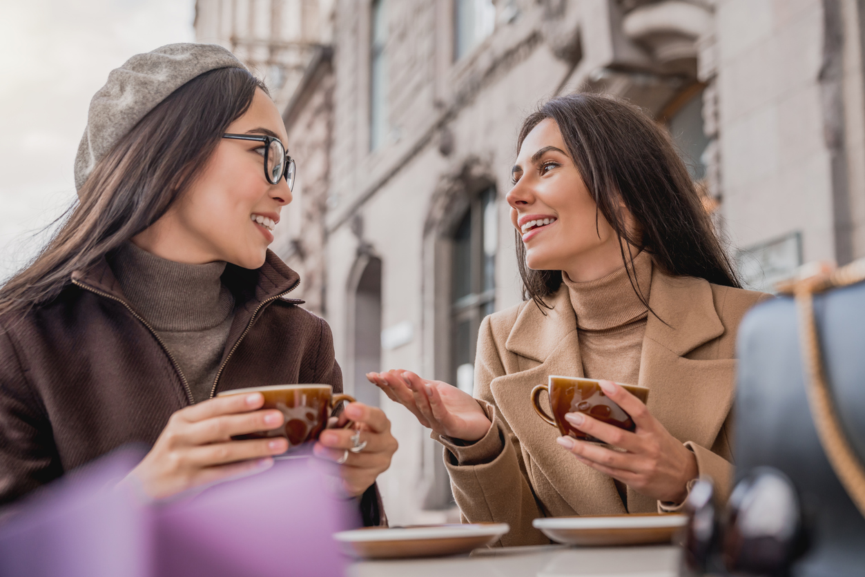 Two young beautiful women talking in an outdoor cafe with shopping bags and cup of coffee