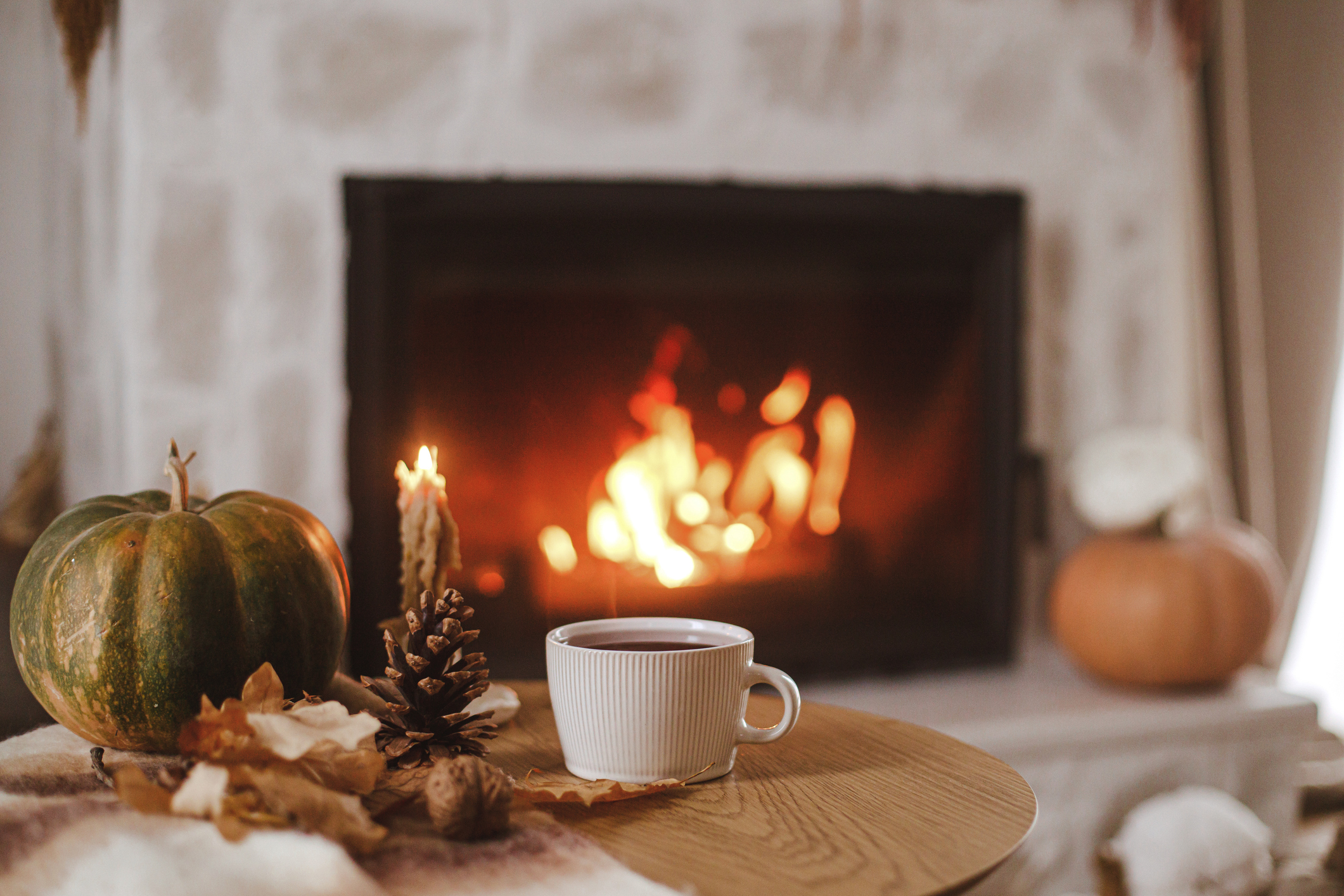 Warm cup of tea, pumpkin, autumn leaves on wooden table on background of burning fireplace. Cozy autumn still life. Thanksgiving and Halloween. Fall hygge Warm cup of tea, pumpkin, autumn leaves on wooden table on background of burning fireplace. Cozy autumn still life. Thanksgiving and Halloween. Fall hygge